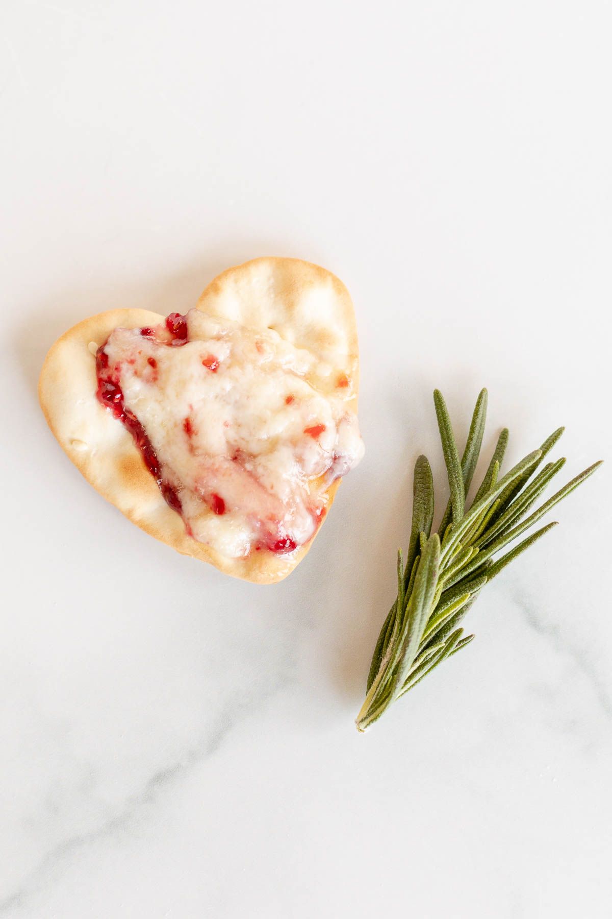 A single heart shaped cracker topped with brie and preserves