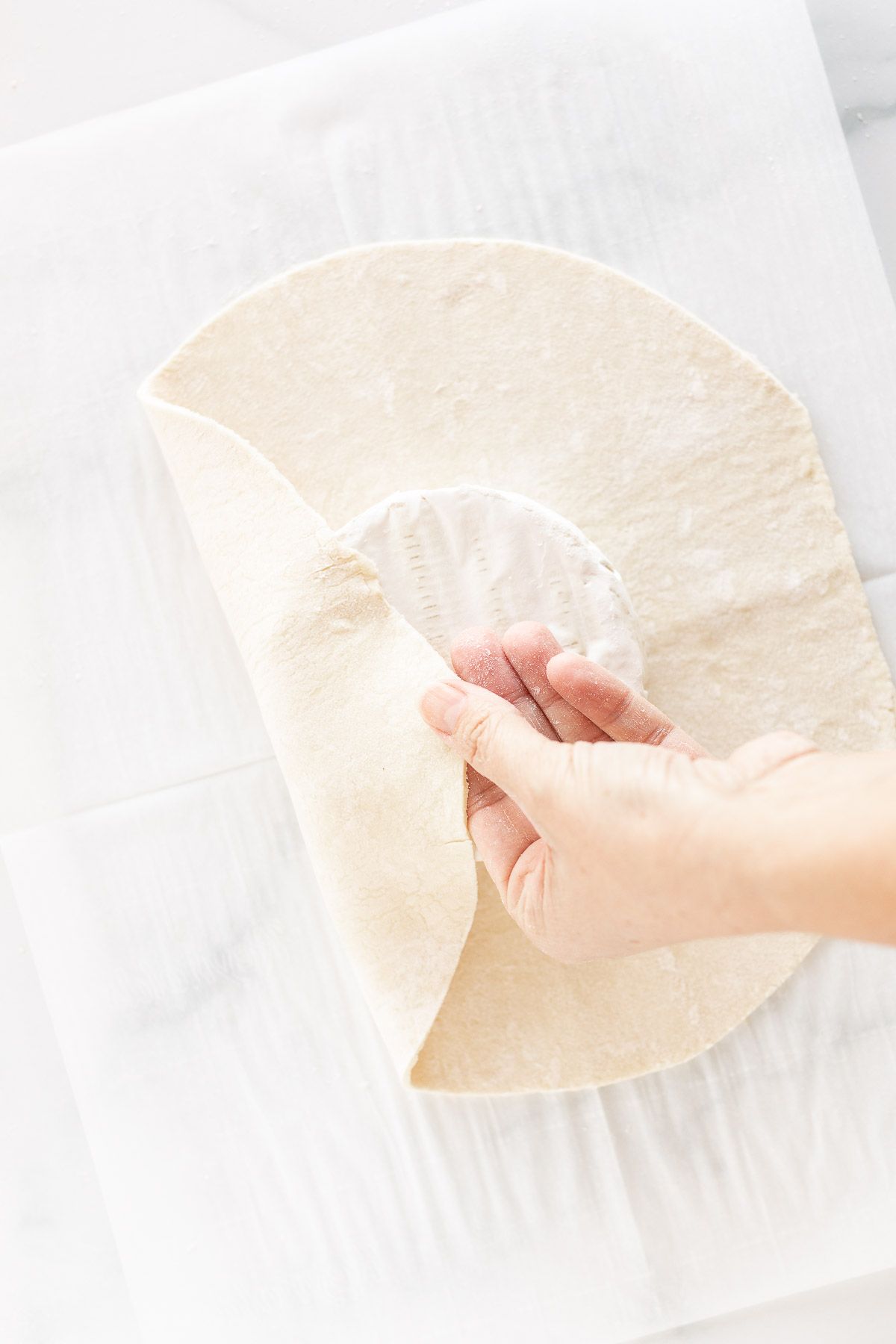 A hand pulling puff pastry over a round of brie