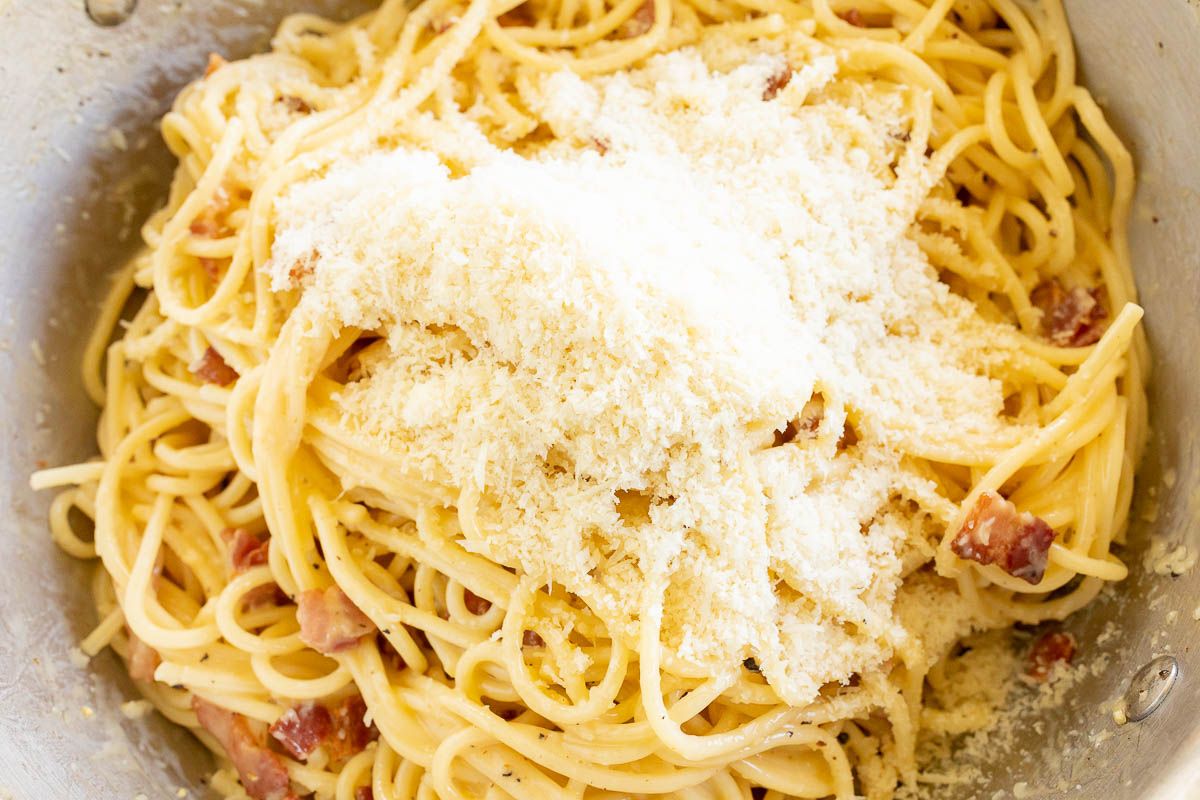 Looking into a silver pot filled with spaghetti carbonara topped with parmesan cheese