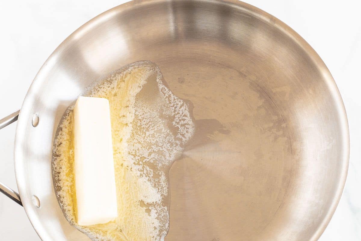 A stick of butter melting in a silver saute pan.