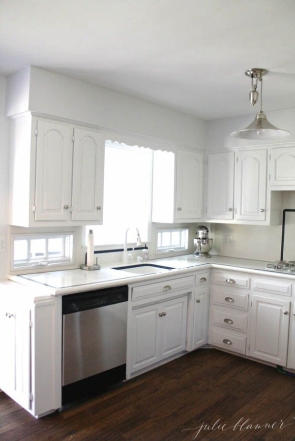 A white kitchen with a wood floor and stainless steel appliances.