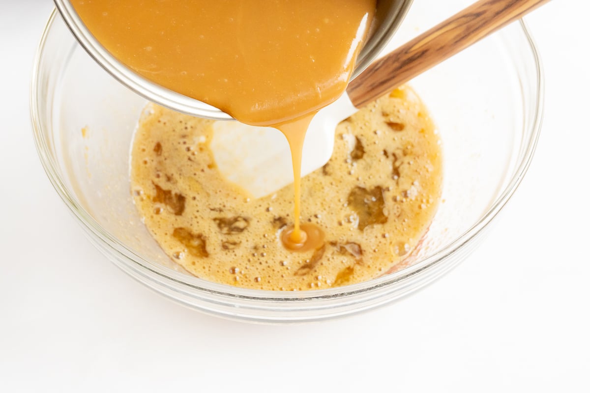 Caramel sauce being poured into a glass bowl for a caramel pecan pie recipe.