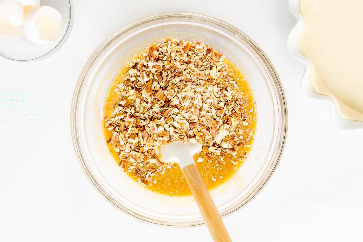 A bowl filled with caramel pecan pie recipe nuts and a wooden spoon.
