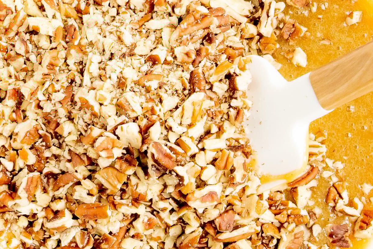 A bowl full of caramel pecans with a wooden spoon.