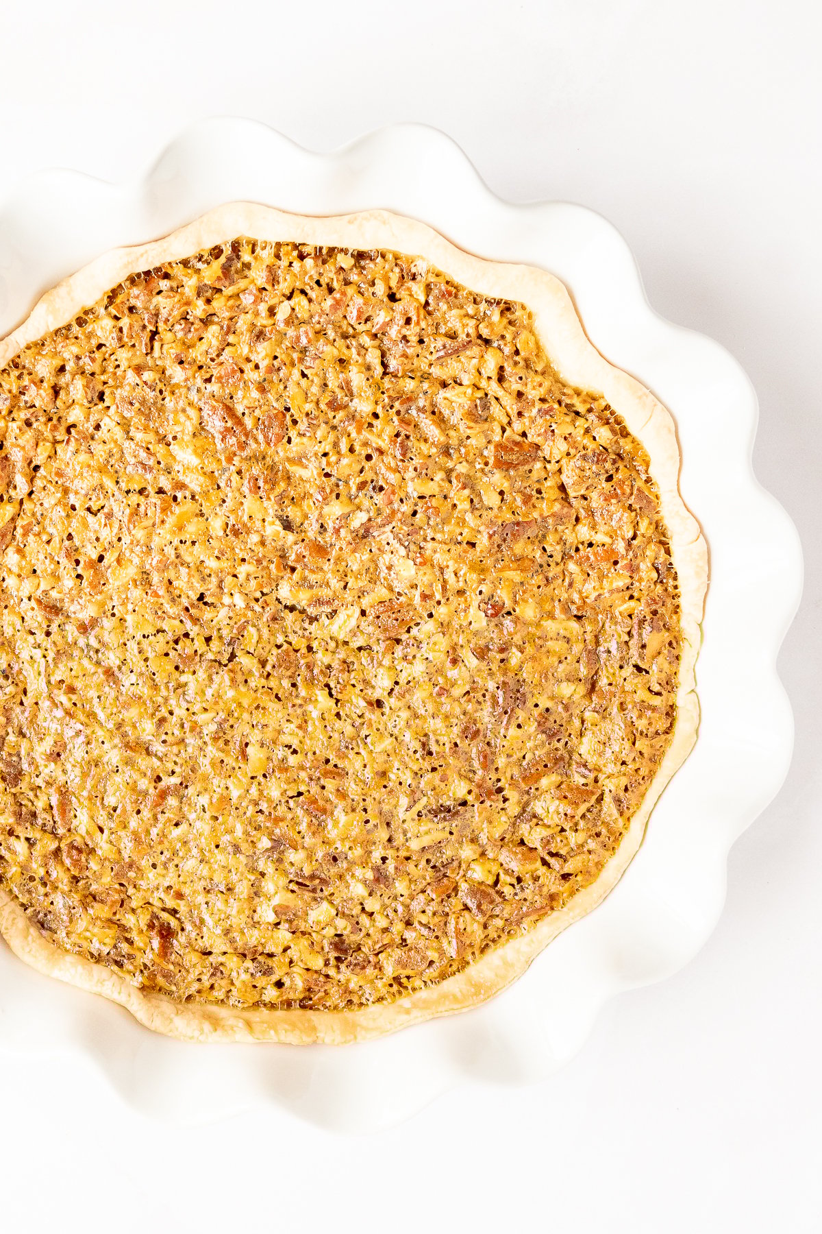 Caramel pecan pie in a white dish on a white background.
