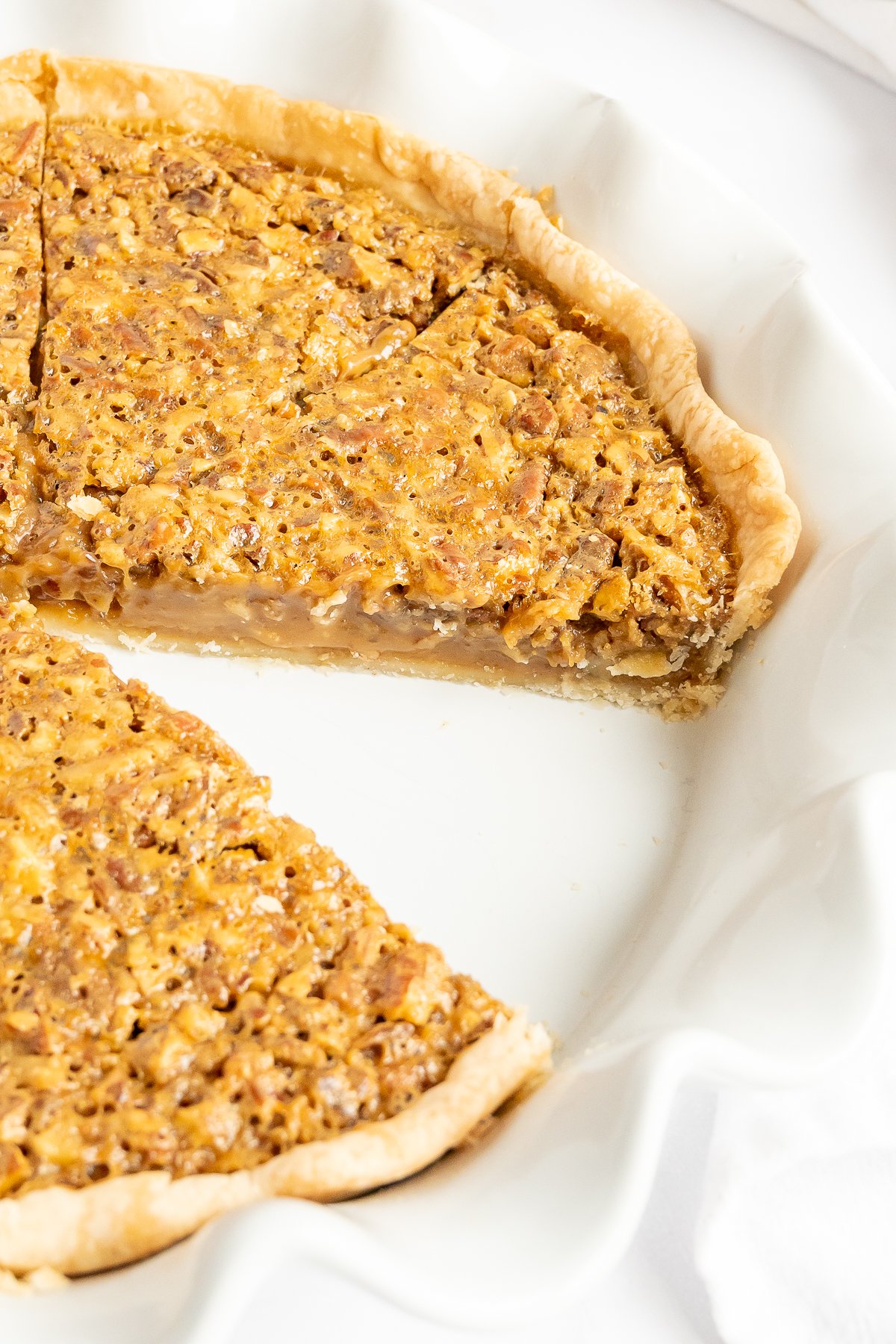 A mouthwatering caramel pecan pie on a white plate with a slice taken out.