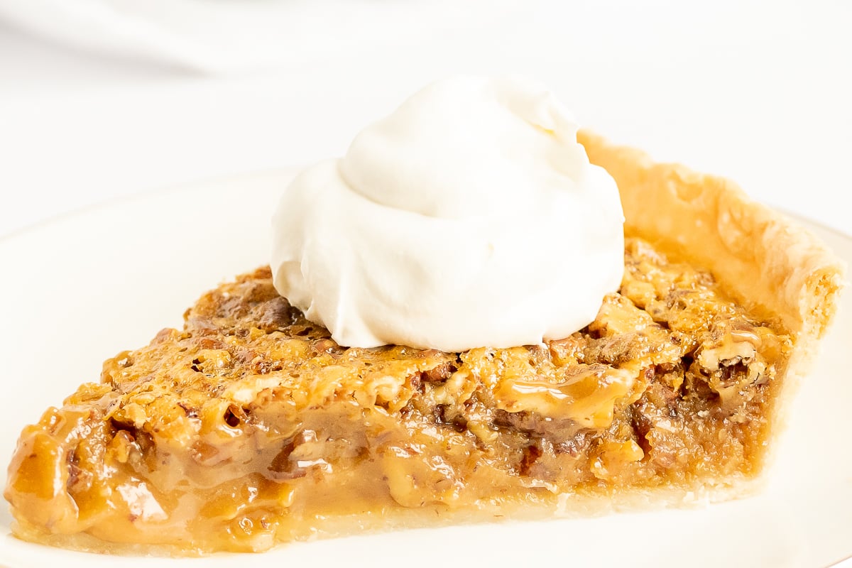 A delicious slice of caramel pecan pie on a plate with whipped cream.