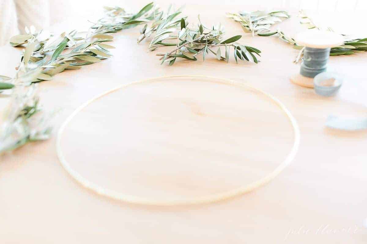 A wood table with a gold hoop and greenery laid out for a DIY wreath.