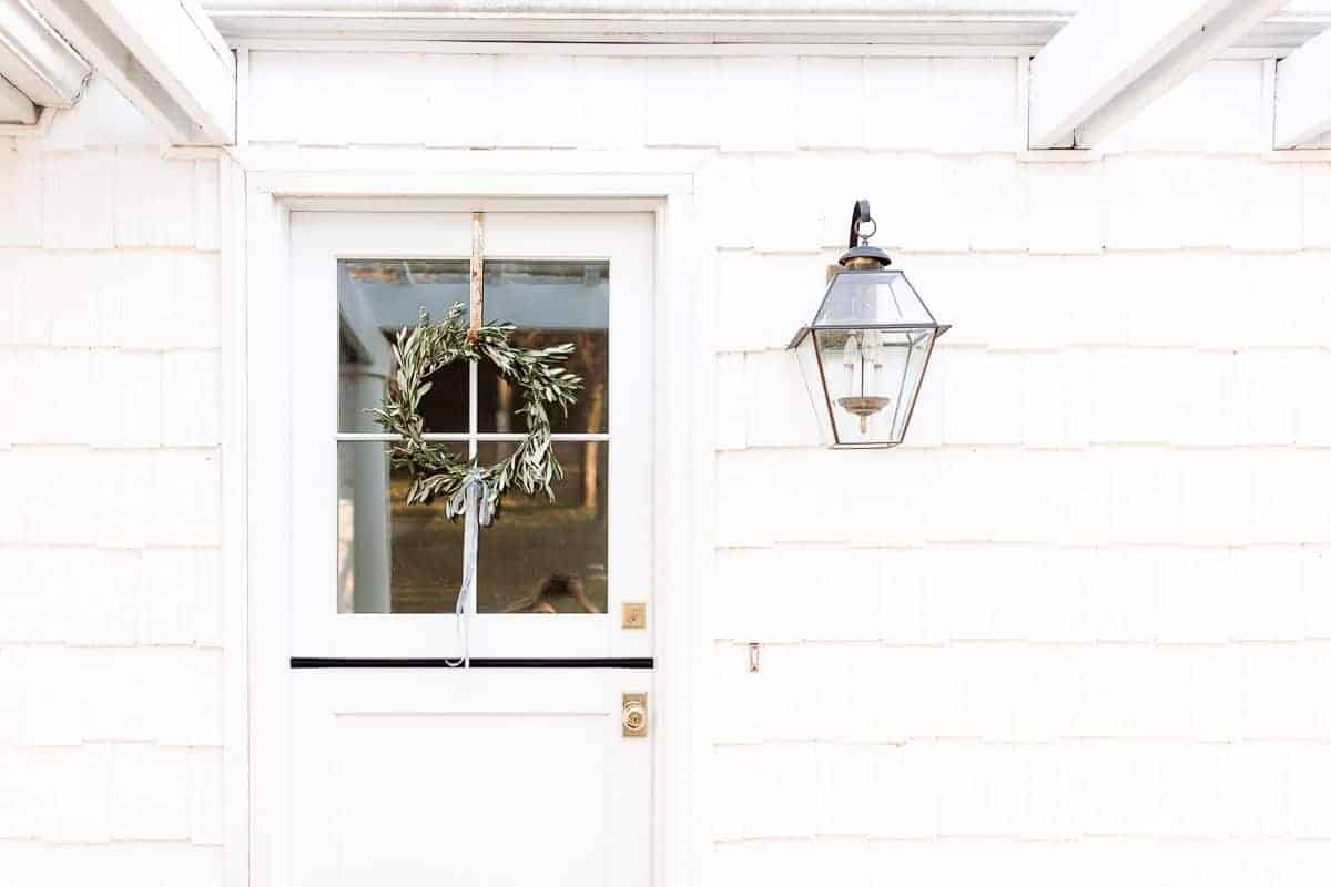 The entryway of a white house with a dutch door, DIY olive wreath hanging on it.