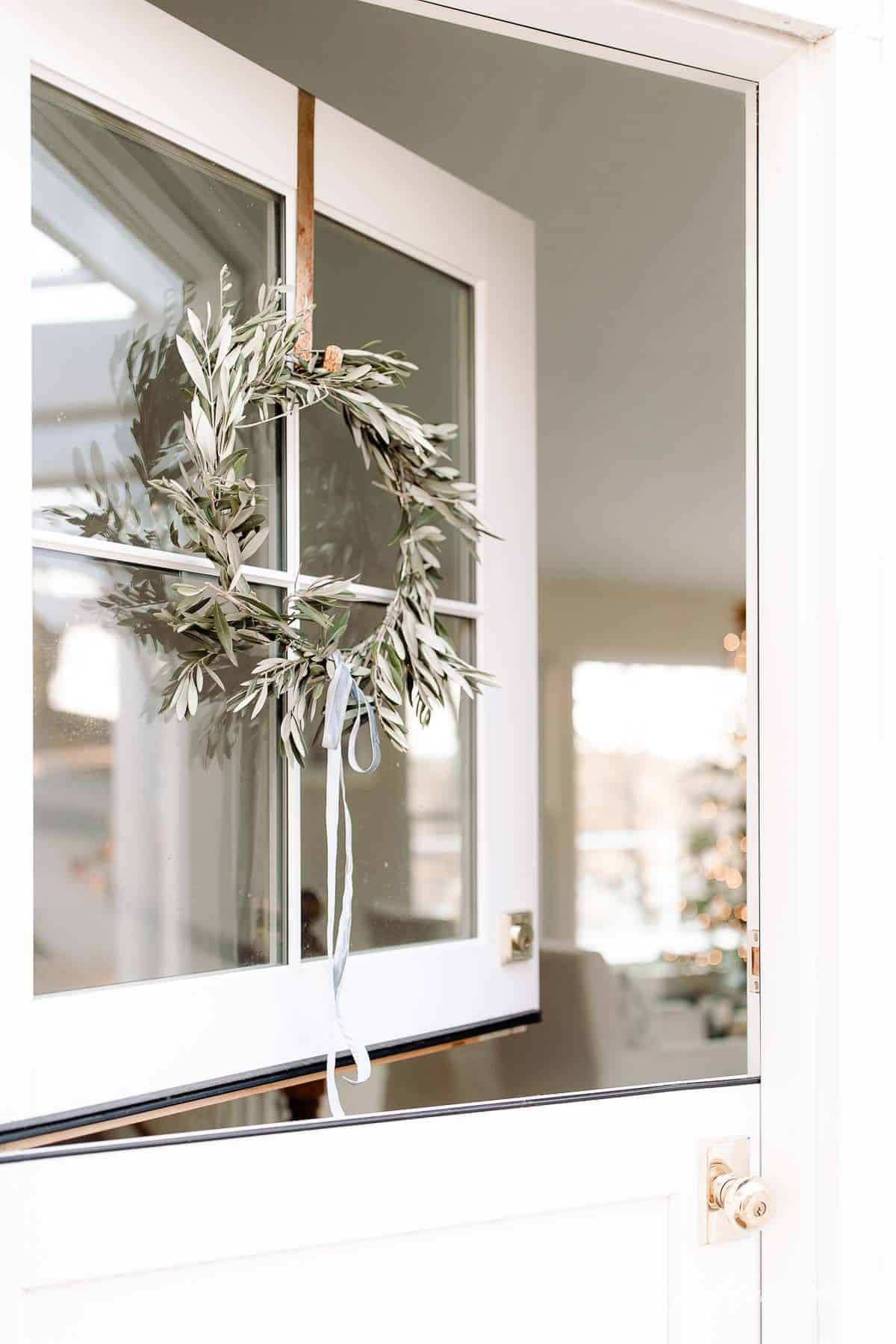 A dutch door with a DIY wreath hanging on the windows, looking into a living room decorated for Christmas.