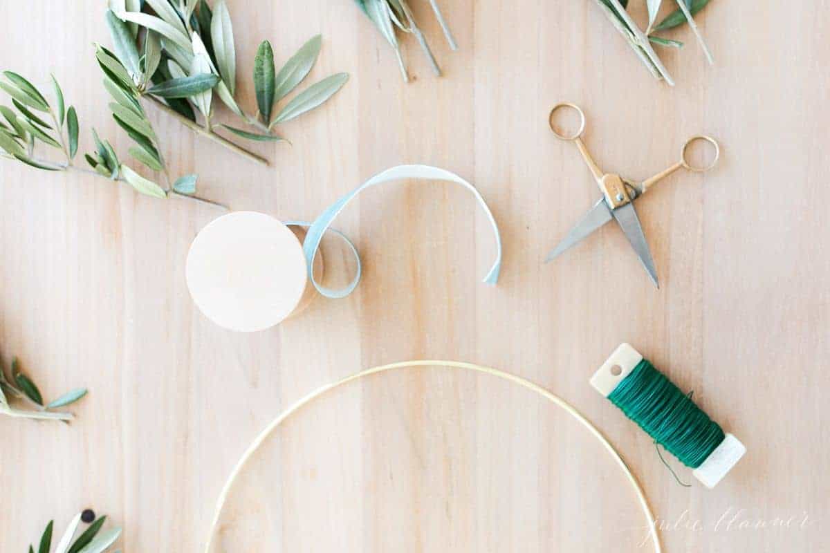 Supplies for a DIY olive wreath laid out on a soft wood surface.