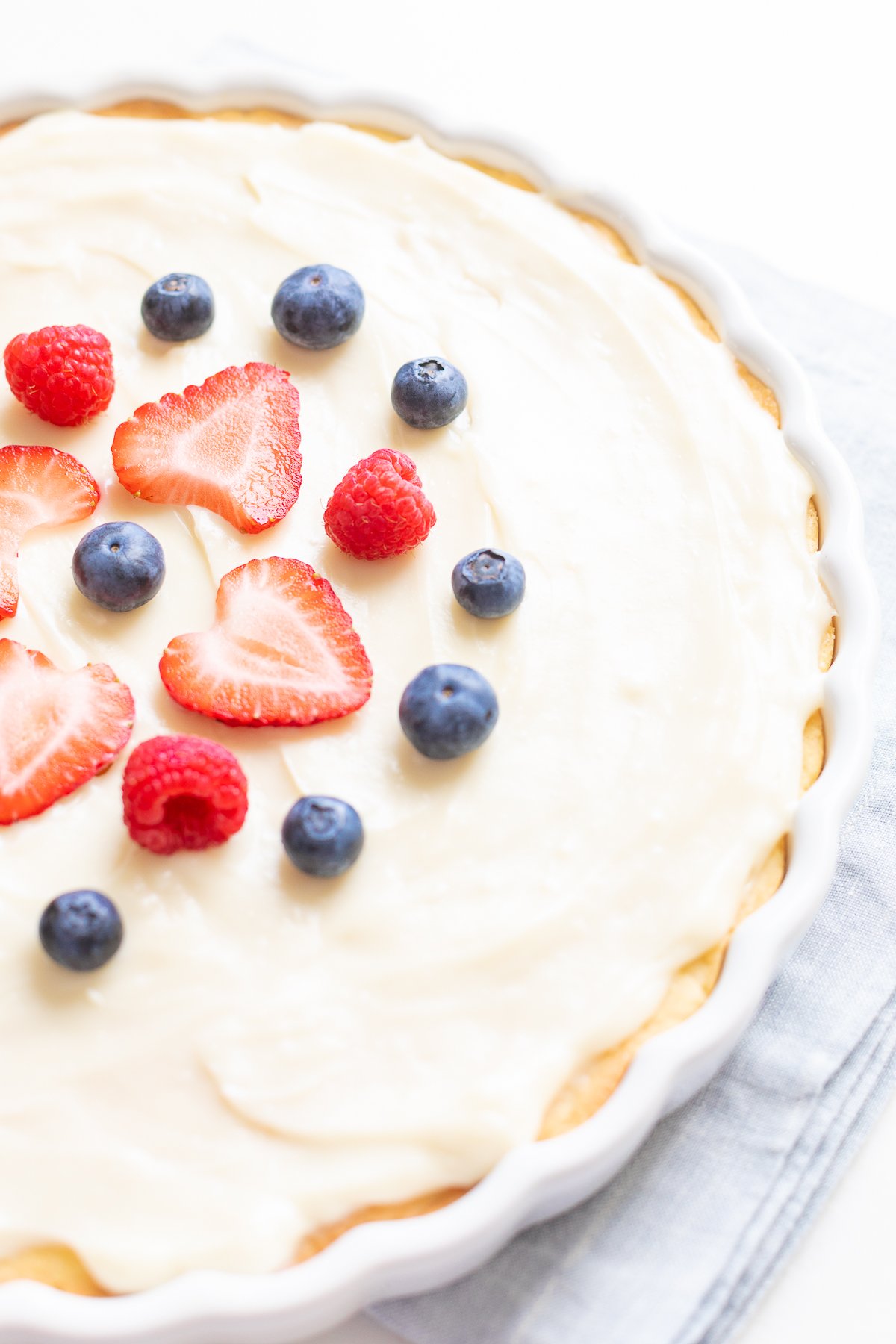 Fresh fruit pizza with cream cheese frosting for the base, garnished with strawberries, raspberries, and blueberries.