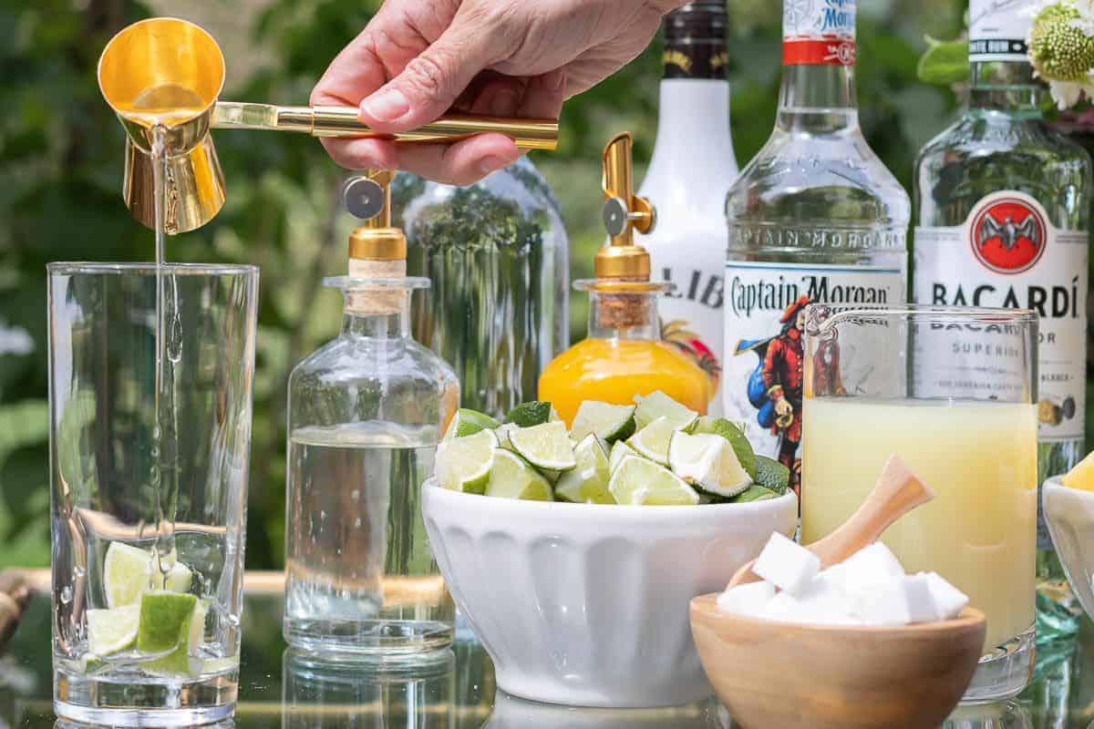 A mojito bar set up on a gold and glass bar cart, a hand reaching over to pour rum in a glass.