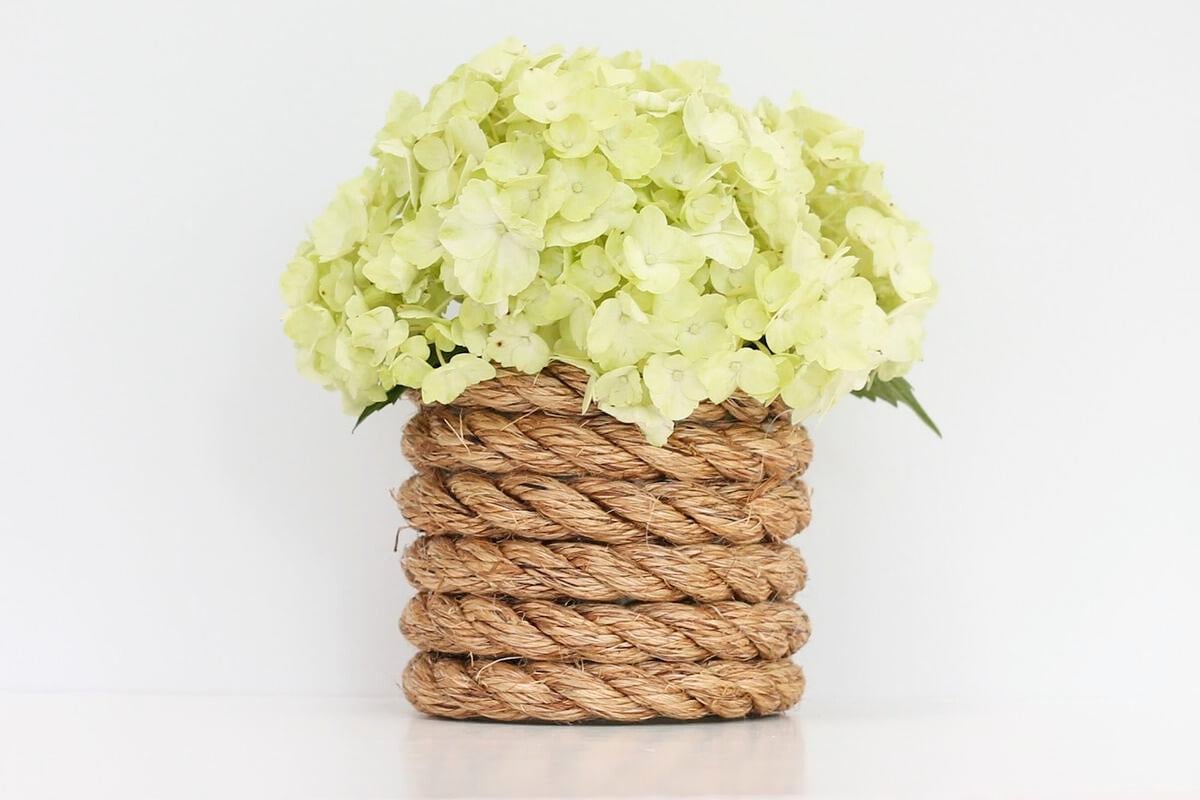 A nautical rope vase with white hydrangea inside.