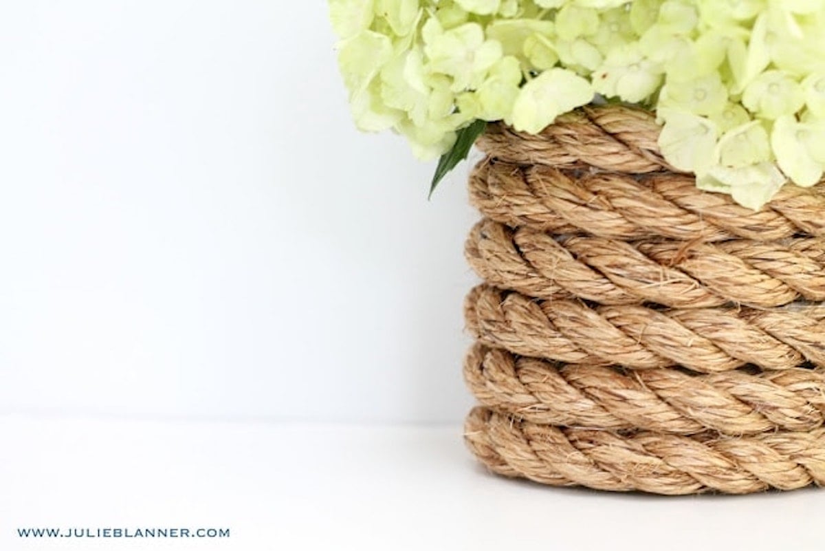 A nautical rope vase with white hydrangea inside.