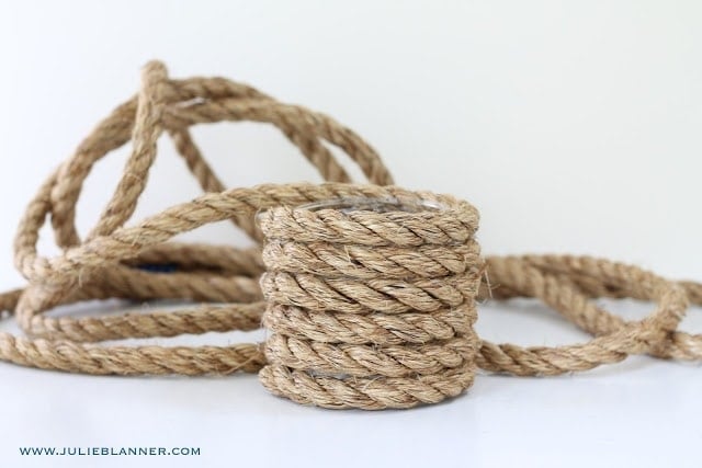 A glass vase being wrapped in a thick rope on a white surface. 