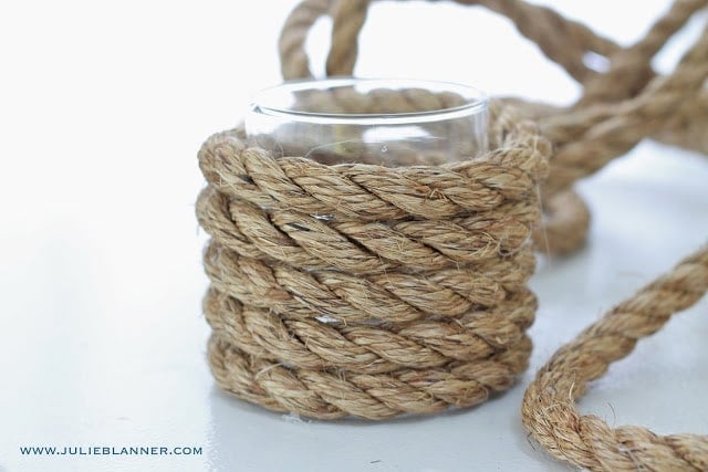 A glass vase being wrapped in a thick rope on a white surface. 