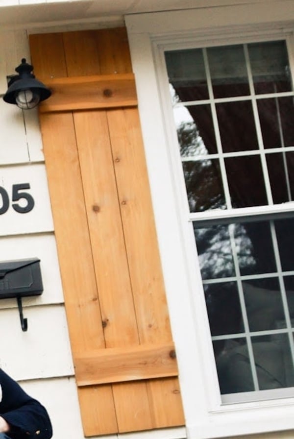 A man standing in front of a house holding a cell phone and showcasing his DIY wood shutters.