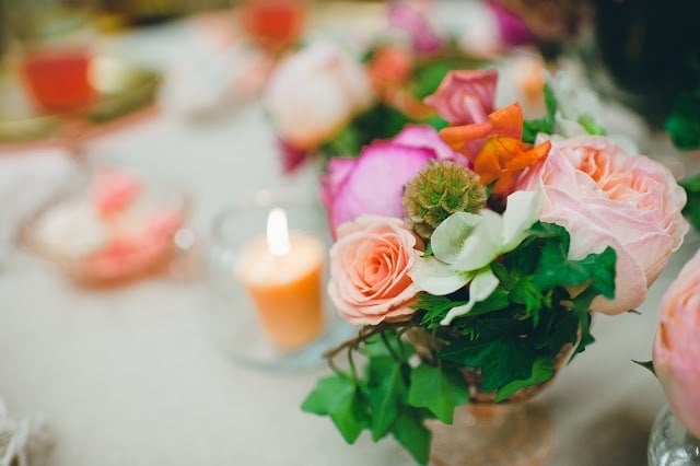 A close up of a pink, orange, green, and purple flowers with a candle to the side