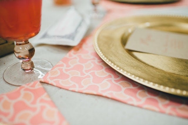 A close up of a gold plate with a coral place mat underneath