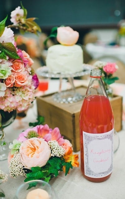 A close up of a pink, orange, green, and purple flowers with a raspberry cocktail to the side.