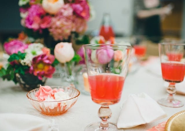 A close up of a pink, orange, green, and purple flowers with a raspberry cocktail to the side.