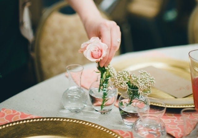 A woman sitting putting pink roses in small, glass vases