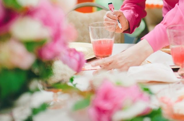 A close up of a pink, orange, green, and purple flowers with a raspberry cocktail to the side.