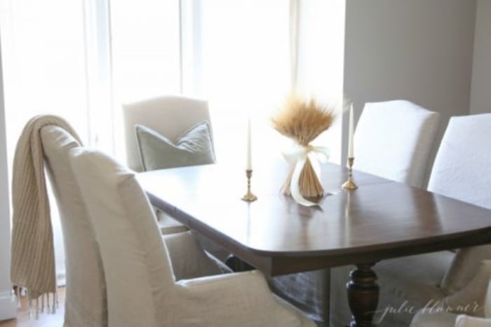 A wheat sheaf tied with ribbon, set on a dark wood formal dining table.