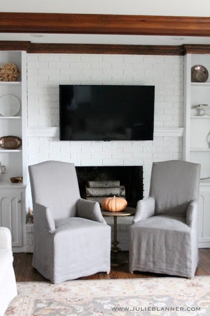 A living room with a white painted brick fireplace, with the tv handing over a mantel to hide tv cords.