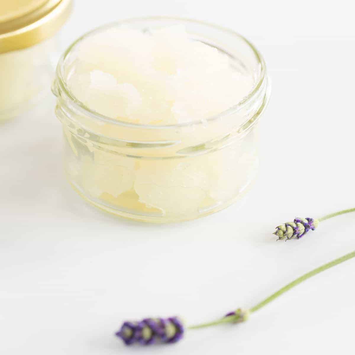 A homemade sugar scrub with lavender, in a glass jar on a white surface.