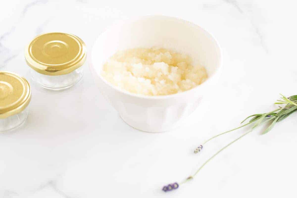 Bowl of sugar and clear glass bottles set out on a white surface, fresh lavender stem in foreground.