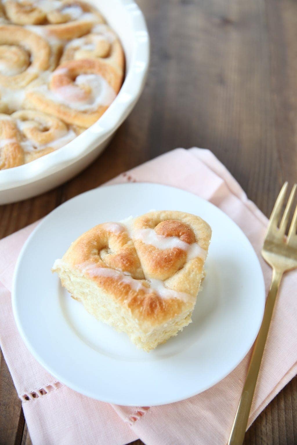 A heart shaped cinnamon roll served on a white plate