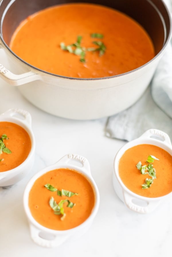 A cast iron pot filled with creamy tomato soup, garnished with fresh basil. Bowls of soup to the side.