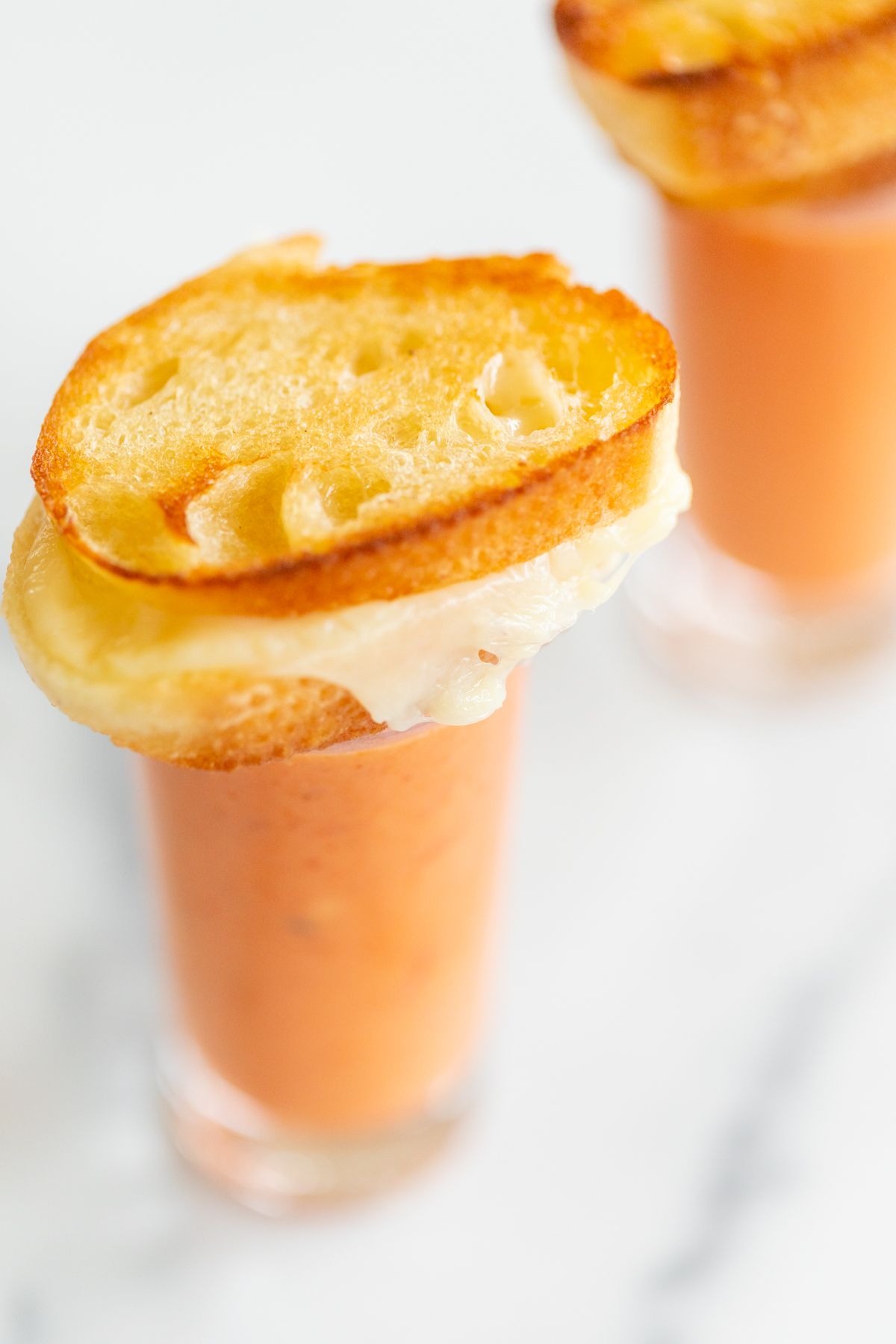 Small glasses with creamy tomato soup, topped with a miniature grilled cheese sandwich.