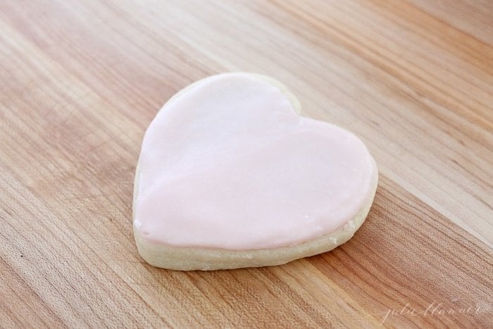 A heart shaped sugar cookie topped with buttercream frosting for sugar cookies on a wooden surface.