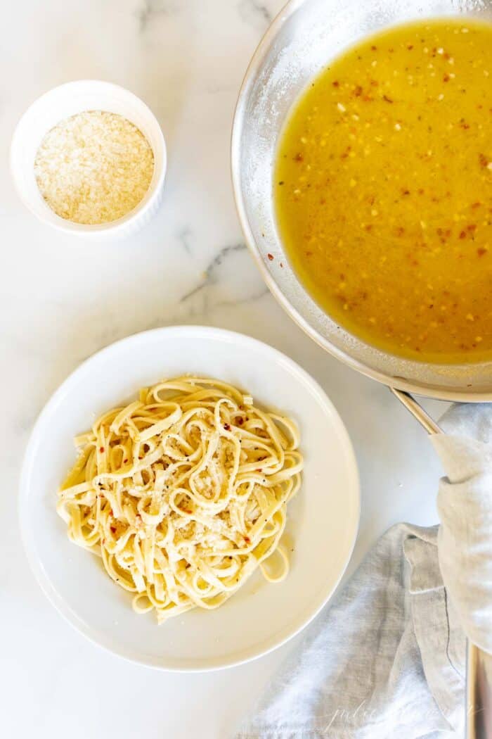 white wine sauce next to plate of pasta and bowl of parmesan cheese