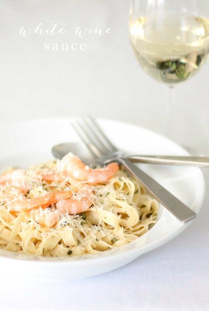 Pasta on a white plate topped with white wine sauce and shrimp. 