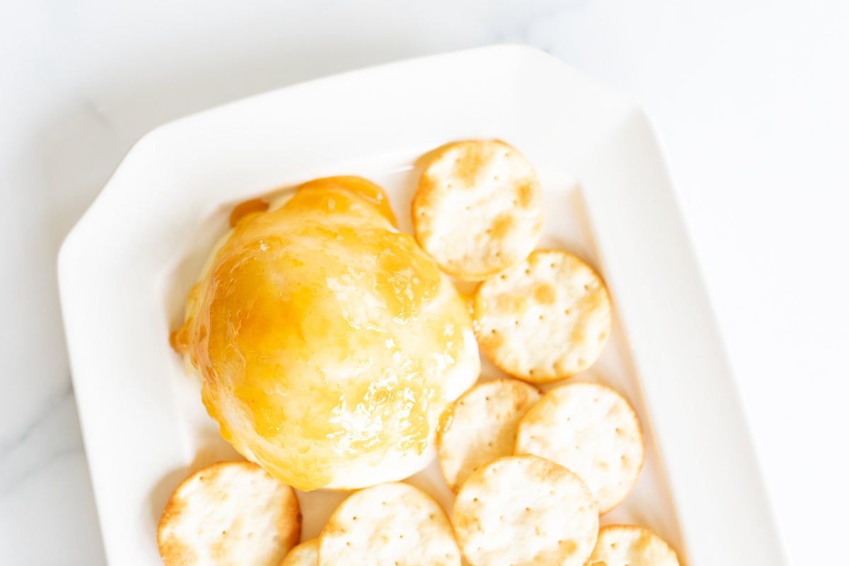 Grilled mozzarella topped with apricot jam, accompanied by round crackers on a white marble surface.