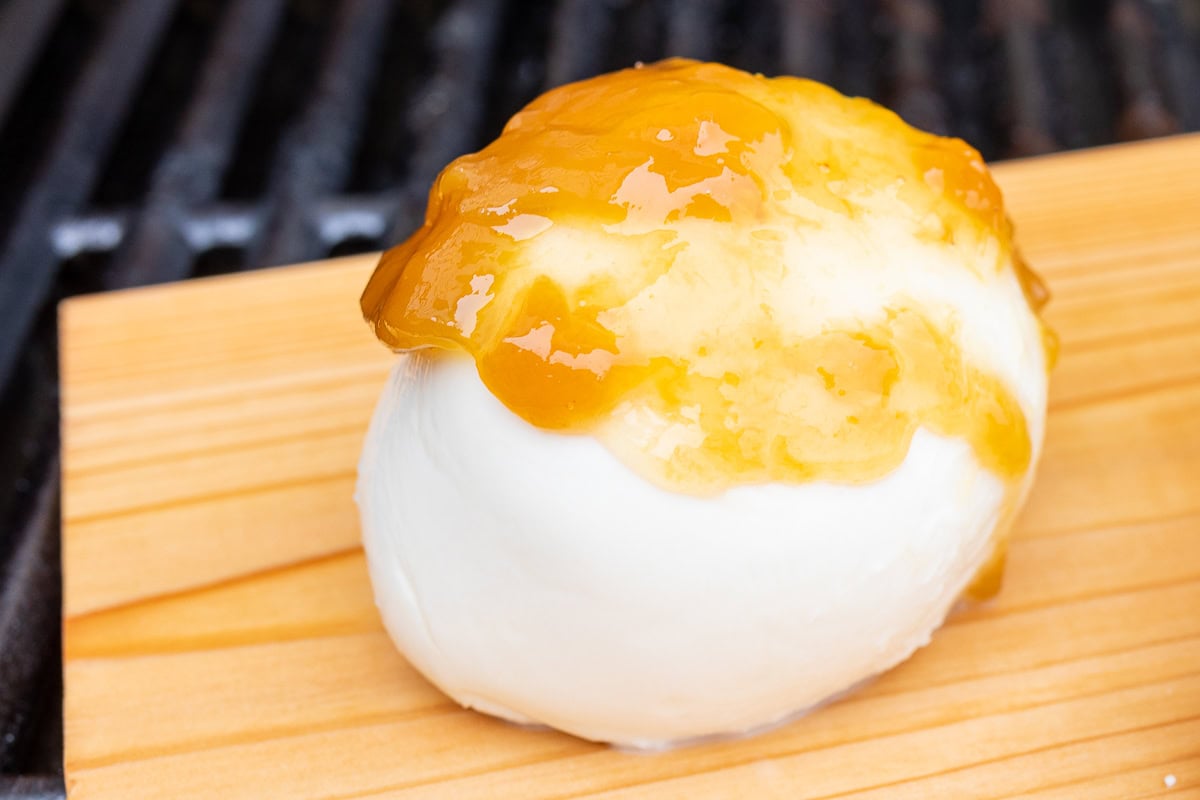 A close-up of a grilled mozzarella cheese appetizer topped with a dollop of orange marmalade, placed on a wooden board.