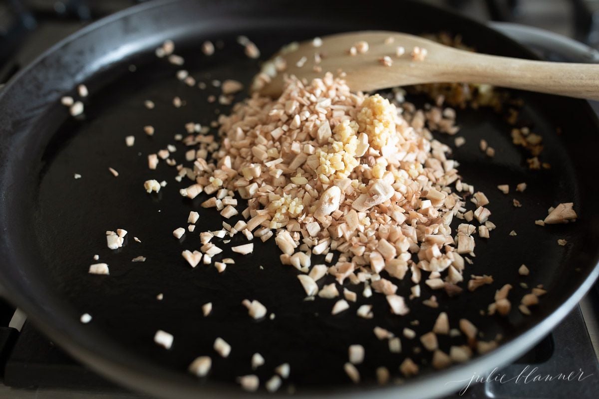 A frying pan full of diced bacon and onions with a wooden spatula to the side.