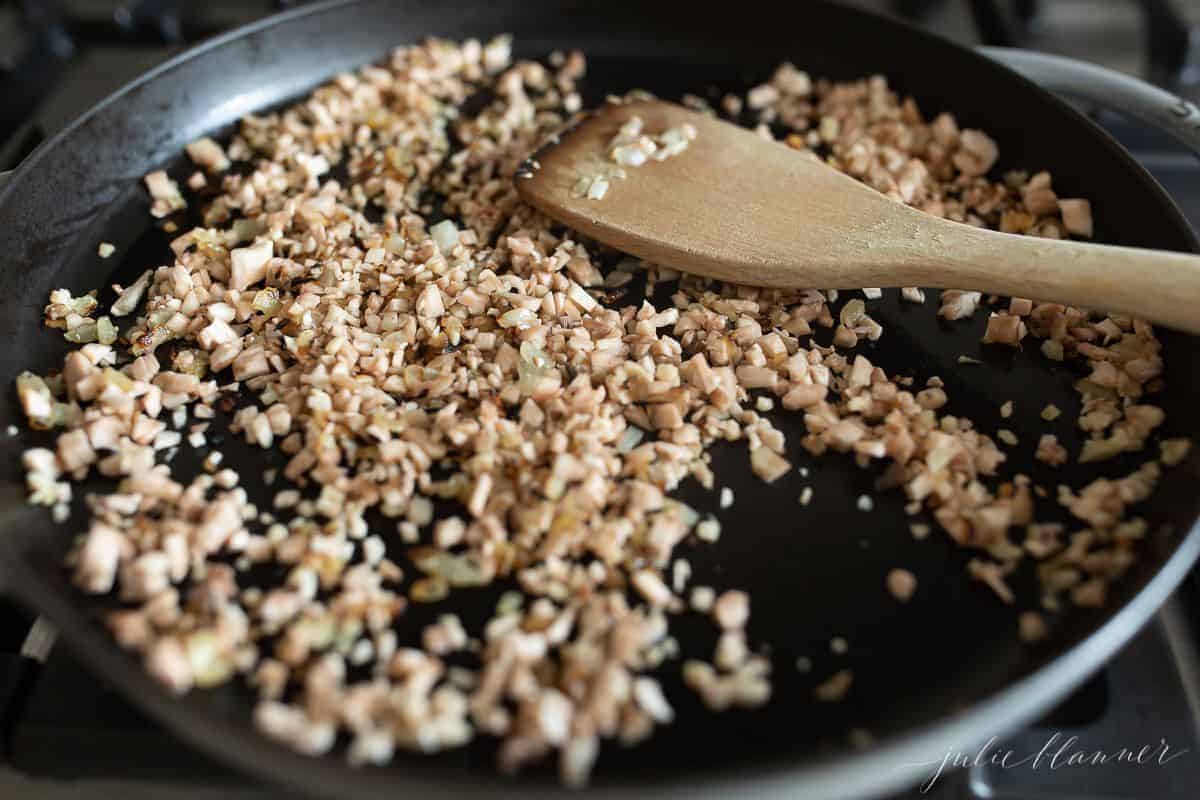 A frying pan full of diced bacon and onions with a wooden spatula to the side.