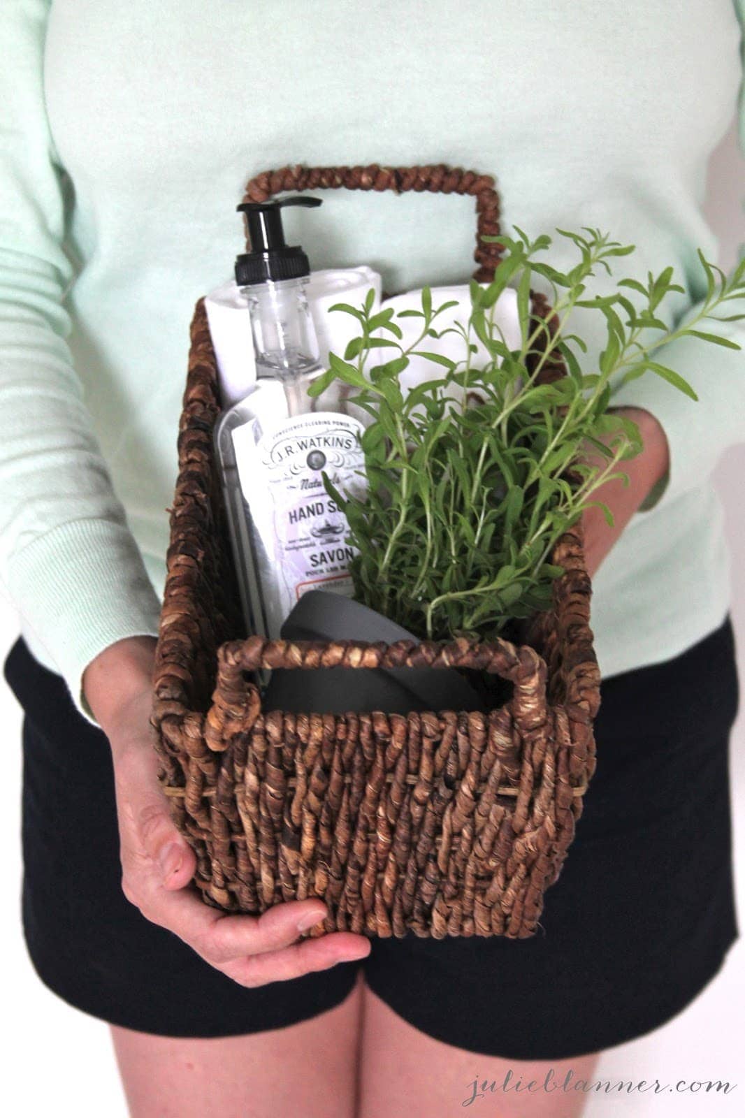 A woman in a green shirt holding a housewarming gift basket