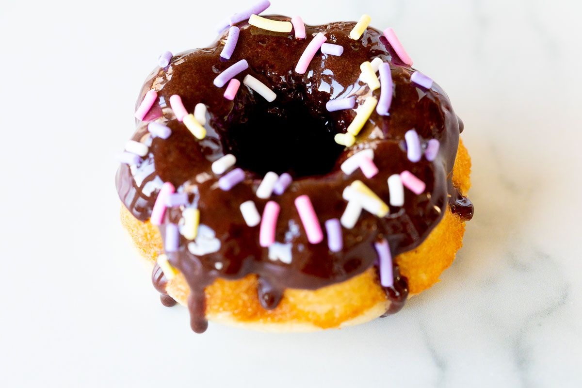 A homemade baked donut covered in chocolate frosting and sprinkles.