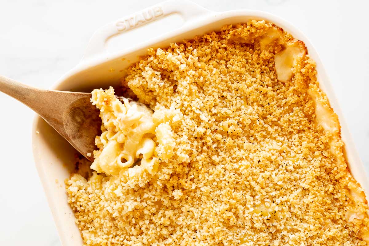 Baked macaroni and cheese in a white dish with a wooden spoon.