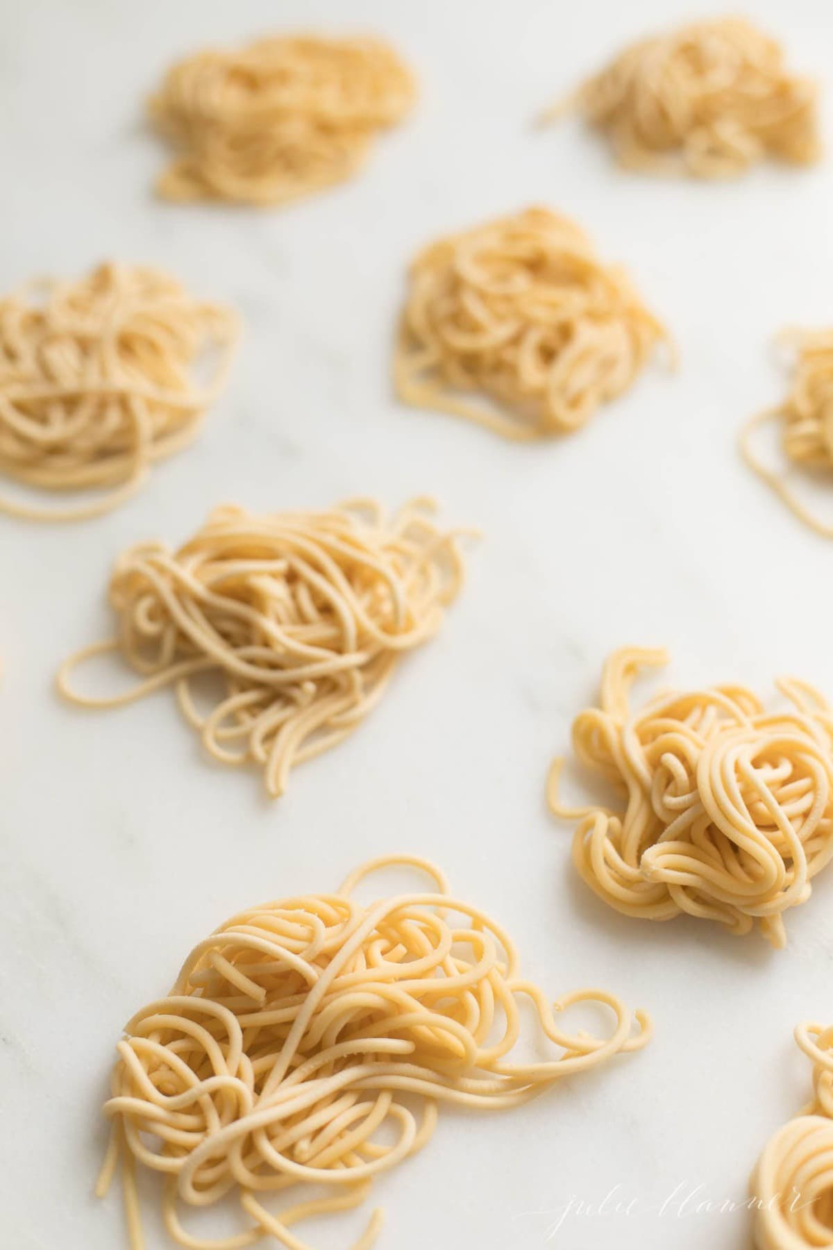 Small piles of freshly made spaghetti style pasta, uncooked on a countertop.