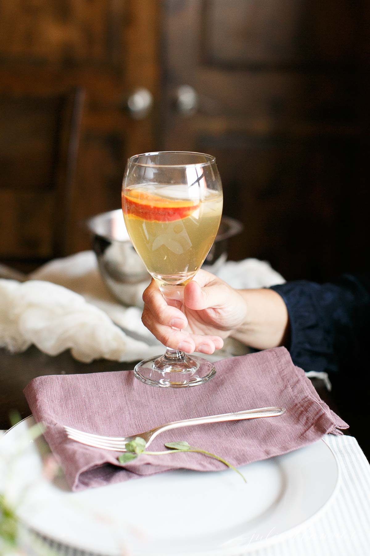 A hand holding a glass of Prosecco sangria over a dining table.