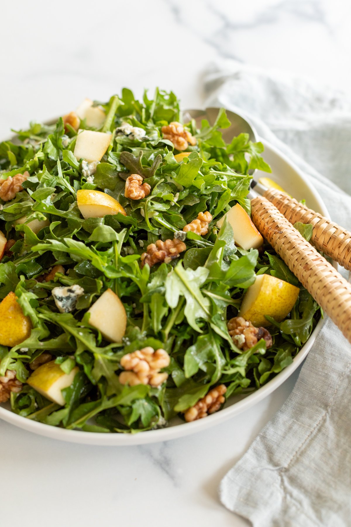 A white bowl full of pear salad, with arugula, walnuts and gorgonzola.