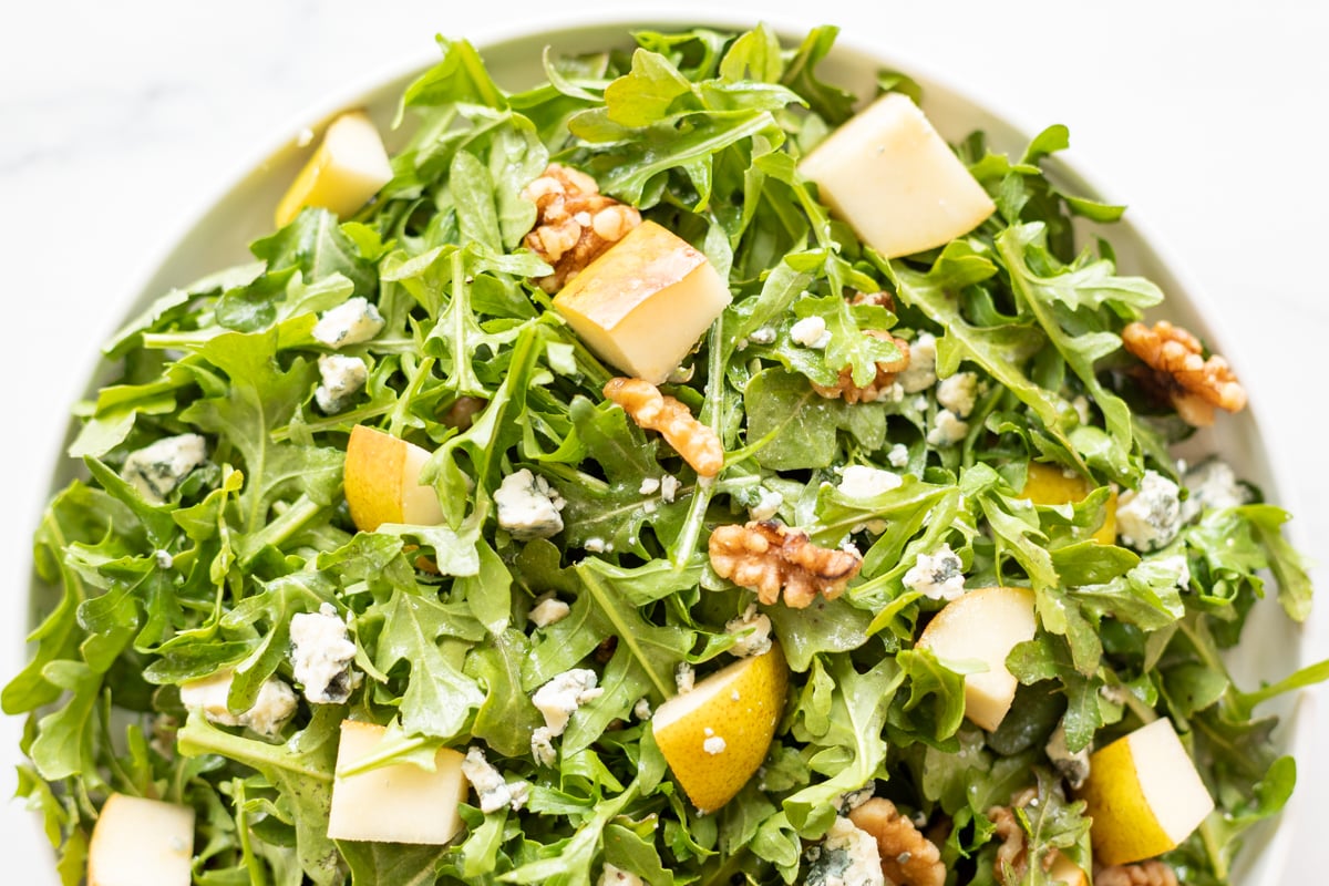 A white bowl full of pear salad, with arugula, walnuts and gorgonzola.