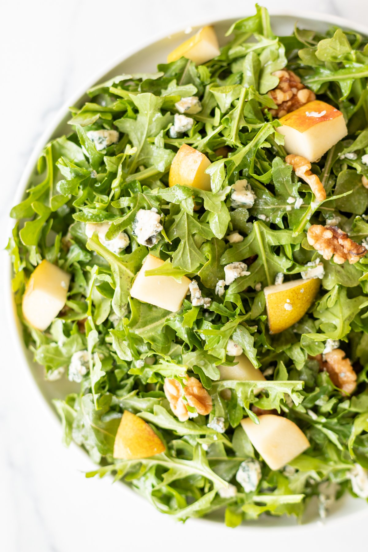 A white bowl full of pear salad, with arugula, walnuts and gorgonzola.